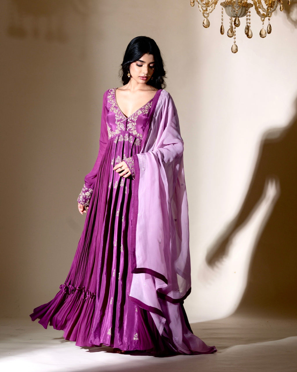 Woman wearing a purple evening gown with a matching shawl in a softly lit room.