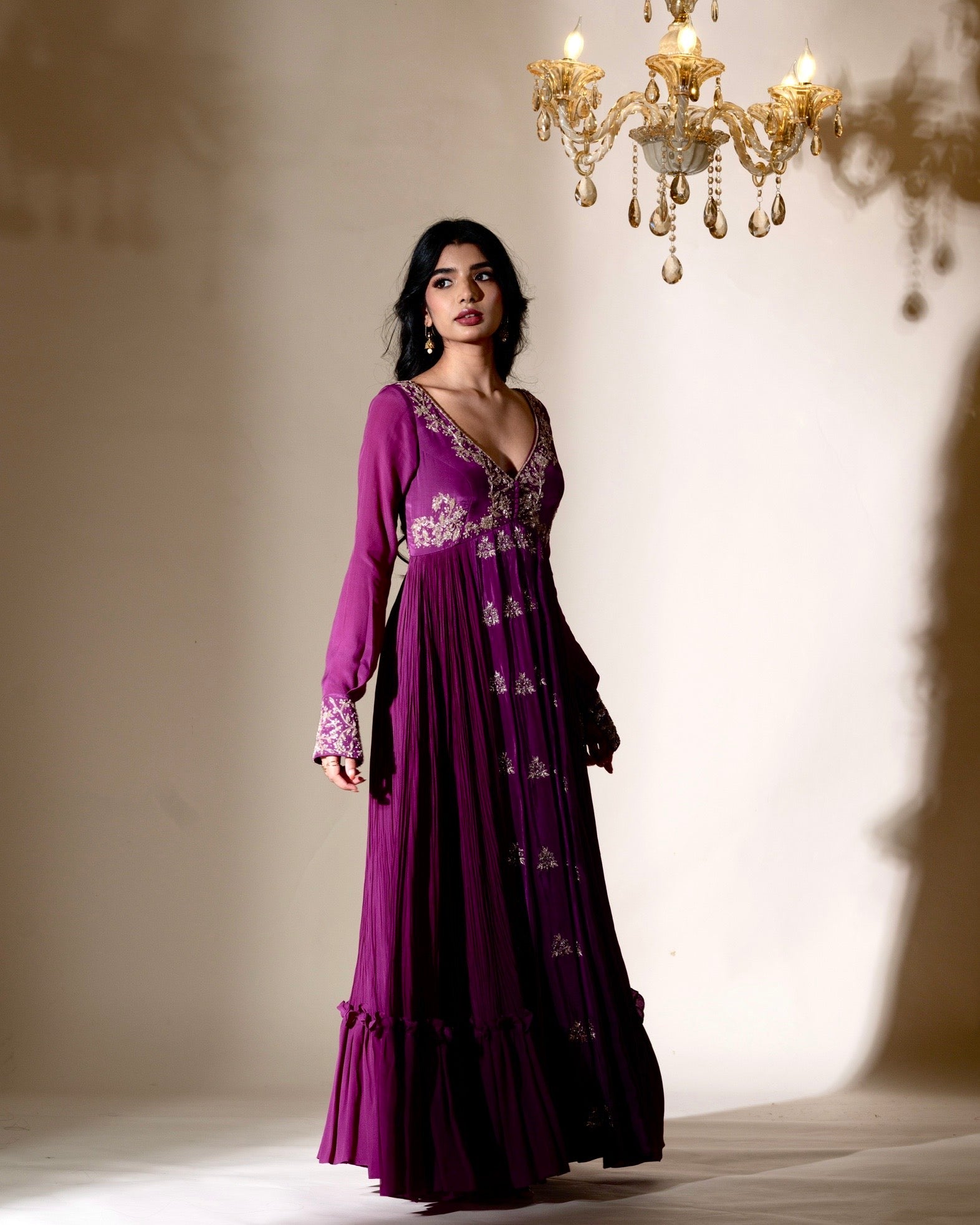 Woman wearing a purple dress with floral patterns in a softly lit room with a chandelier.