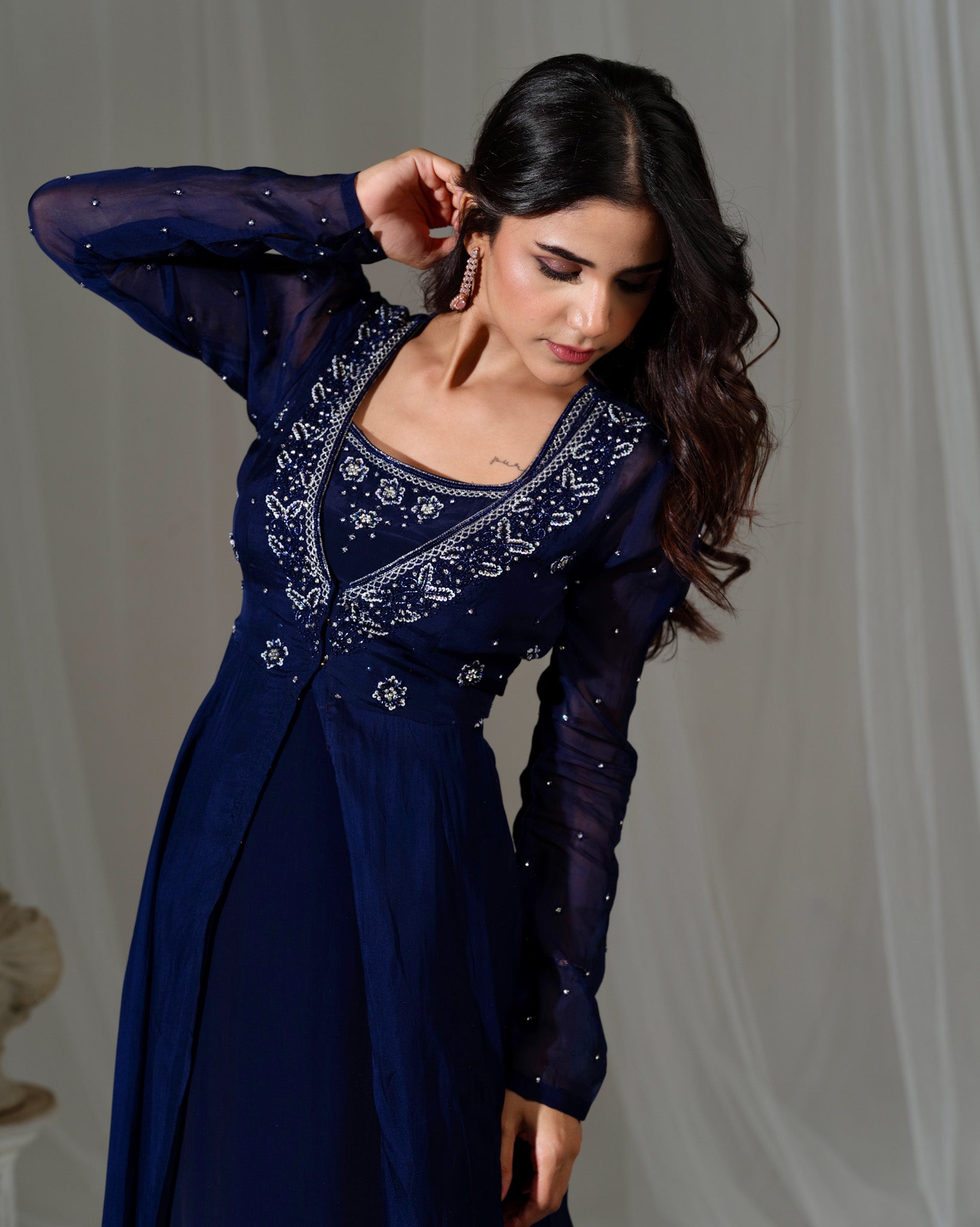 Woman wearing a dark blue embroidered dress against a plain background