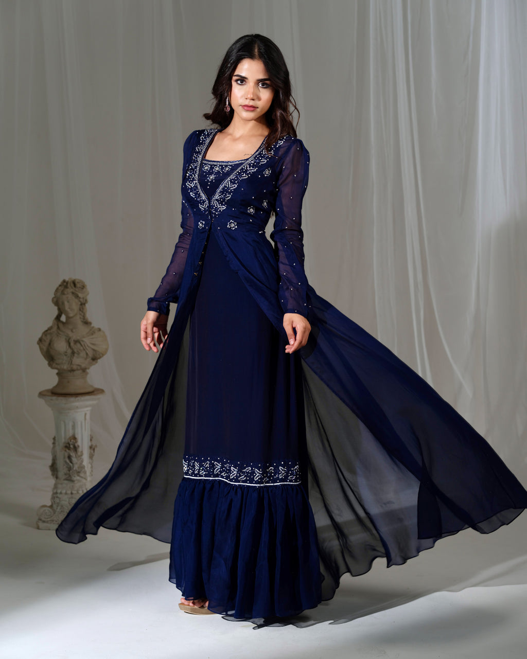 Woman wearing a long, dark blue embroidered dress against a neutral background