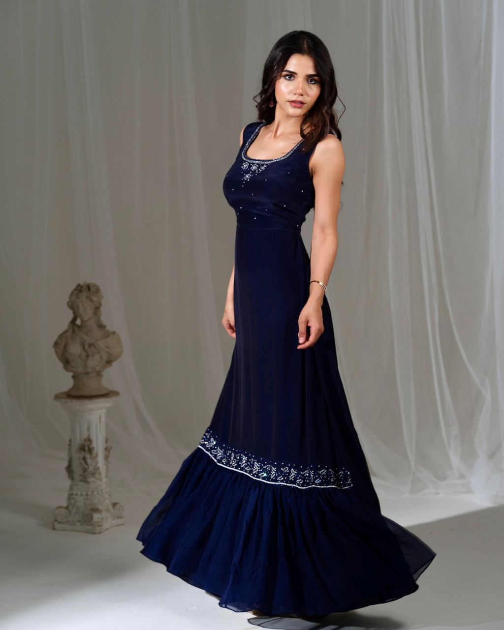 Woman wearing a navy blue evening gown with white embroidery against a white curtain background