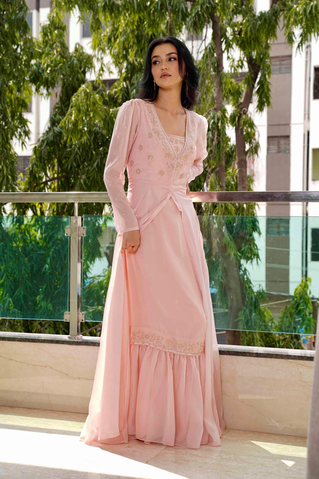 Woman in a pink dress standing on a balcony with greenery in the background