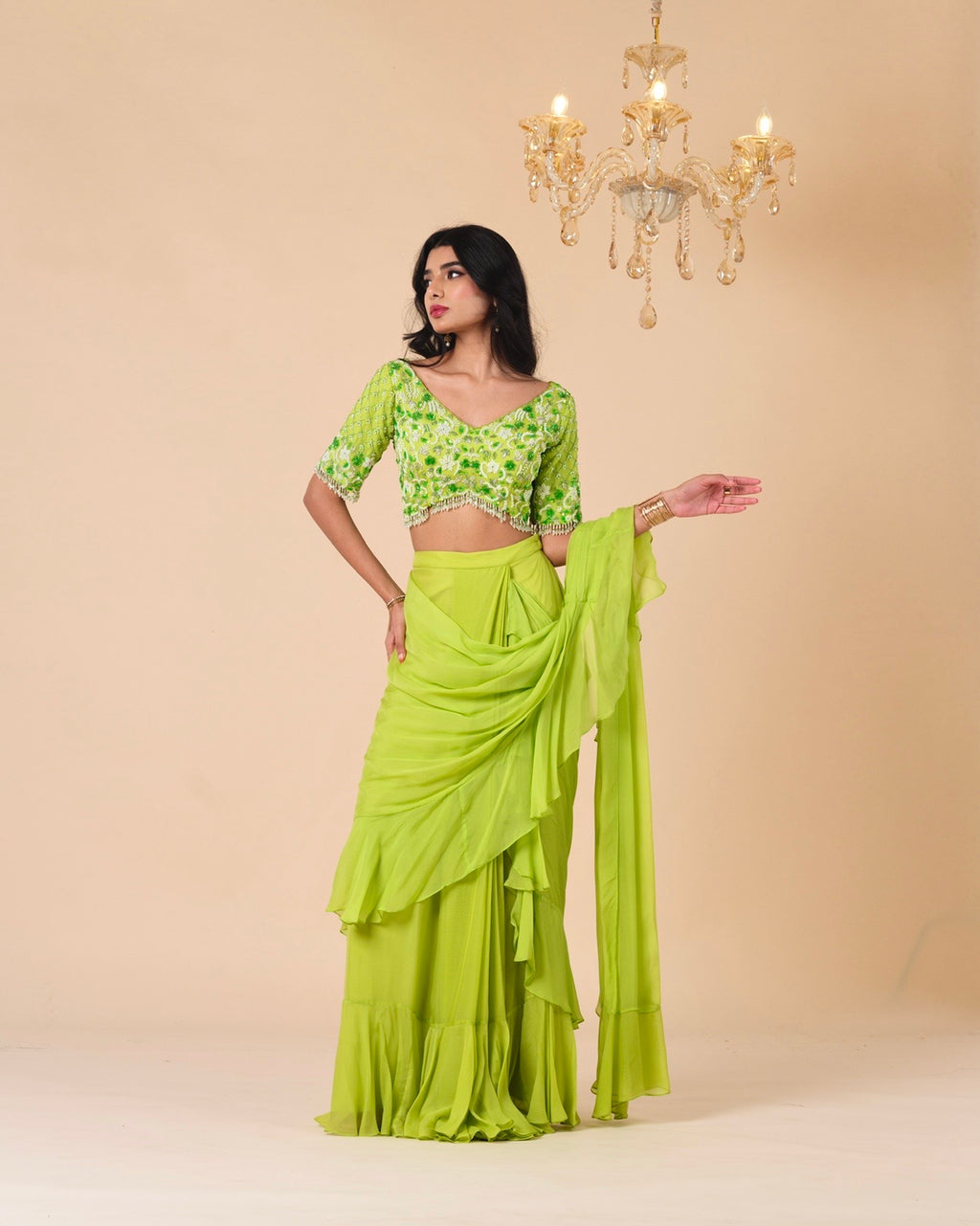 Woman wearing a green saree with a matching blouse against a beige background