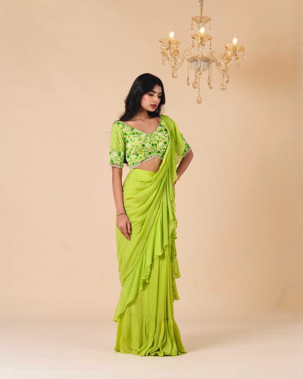 Woman wearing a green saree with a matching blouse against a beige background