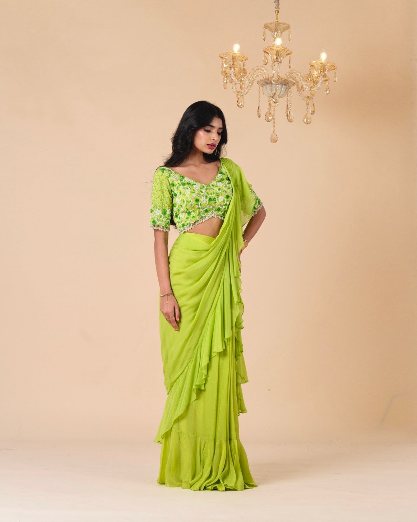 Woman wearing a green saree with a matching blouse against a beige background