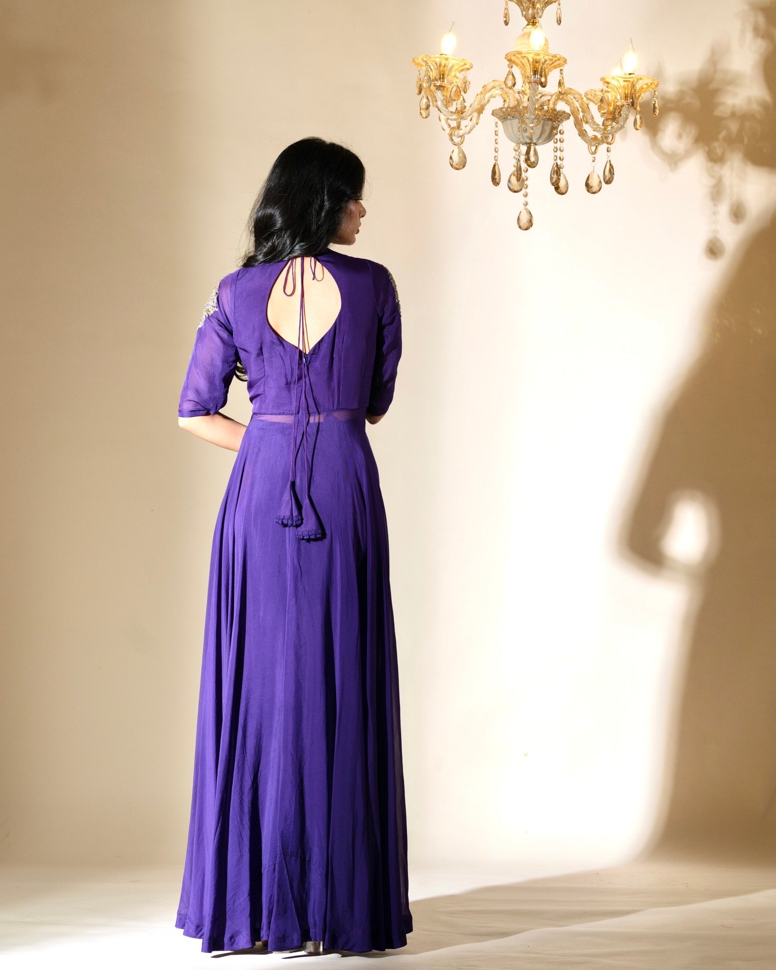 Woman wearing a long purple dress with an open back in a softly lit room.