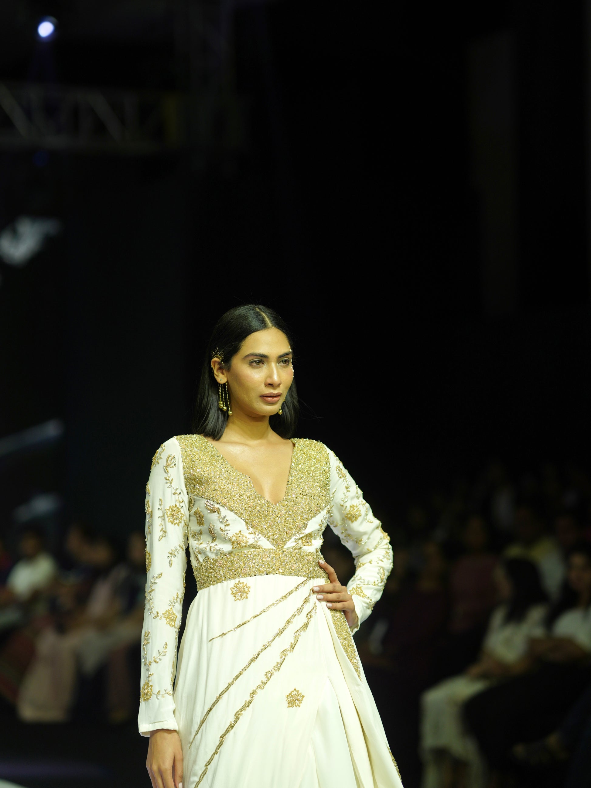 Model wearing a white and gold outfit on a fashion show runway.