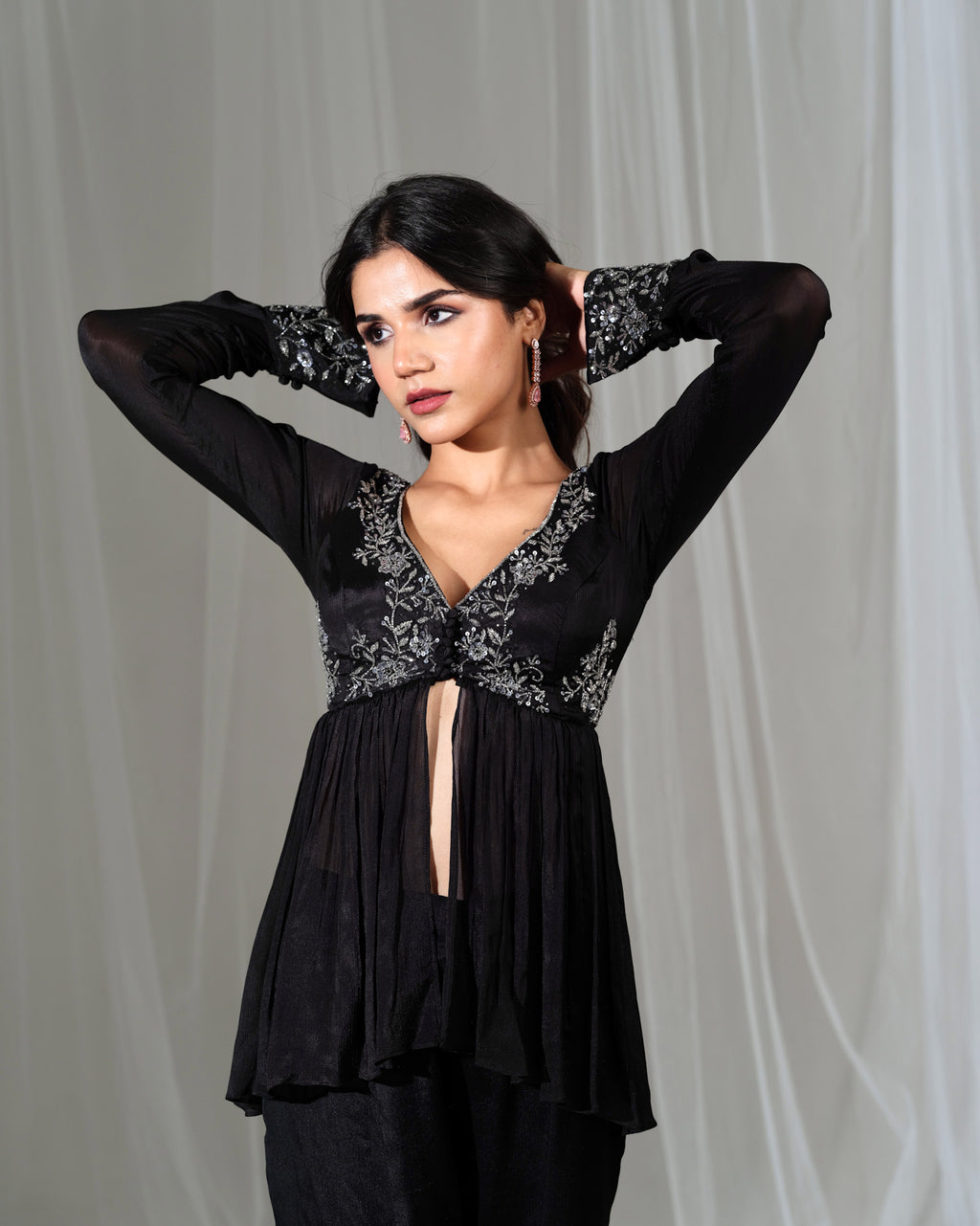 Woman wearing a black blouse with floral embroidery against a gray background