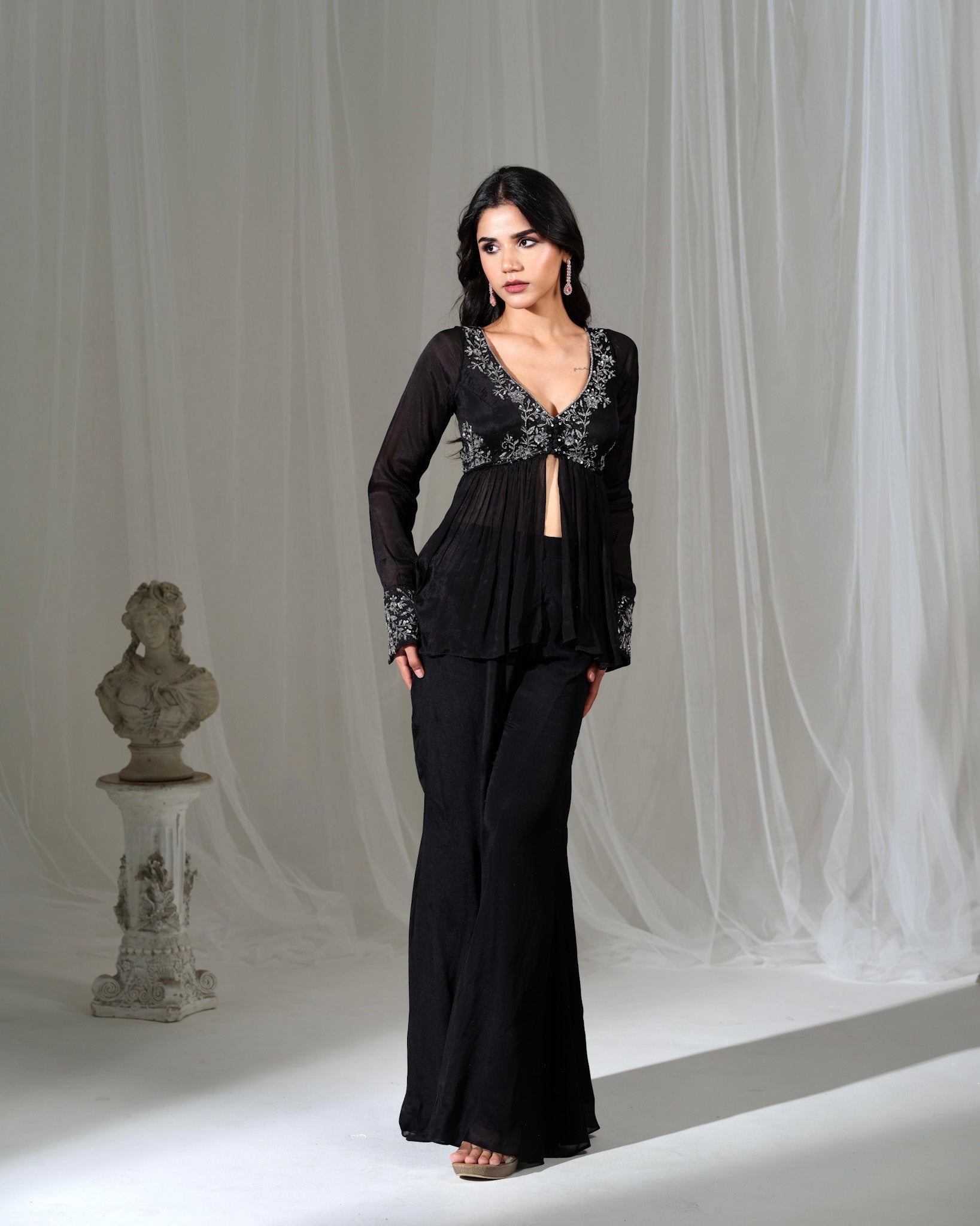 Woman wearing a black evening gown with lace details against a white curtain background