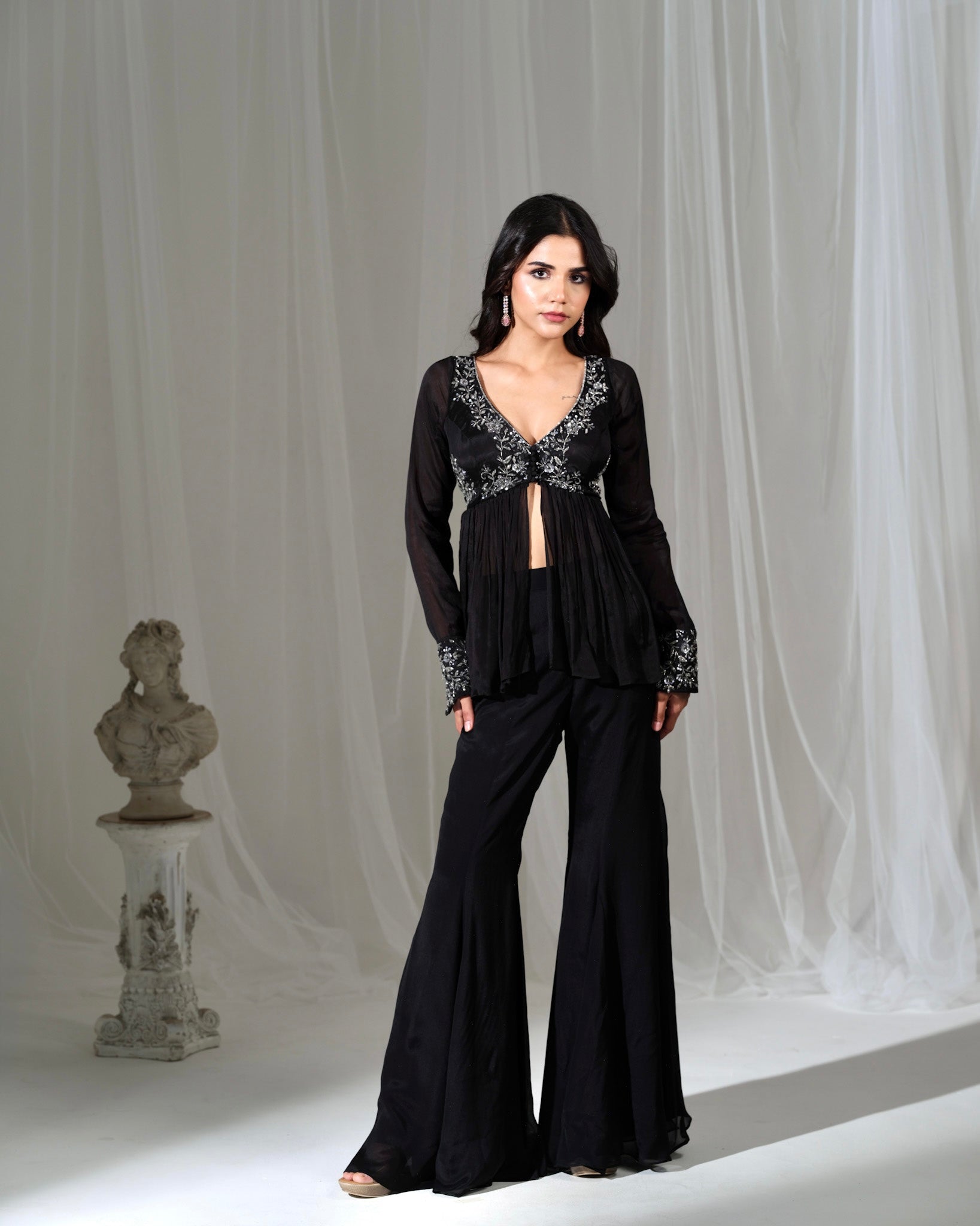 Woman wearing a black outfit with floral embellishments against a gray curtain background