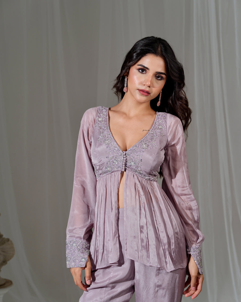 Woman wearing a light purple outfit with intricate detailing against a neutral background