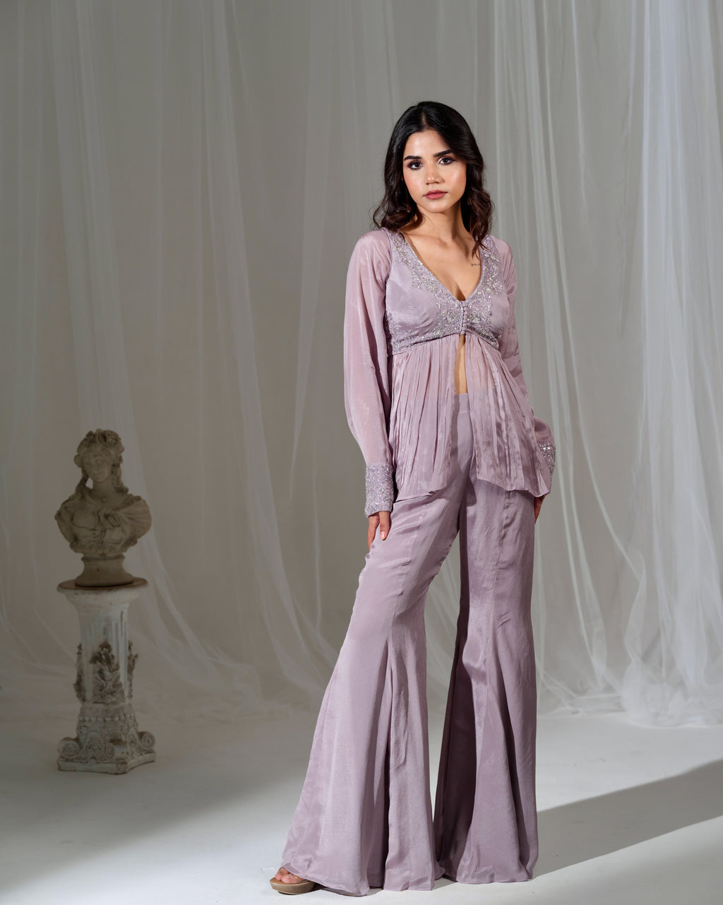 Woman wearing a lavender outfit standing in front of draped fabric