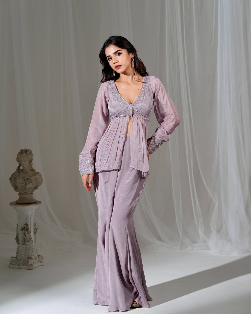 Woman wearing a lavender evening gown with a sheer overlay against a white curtain background