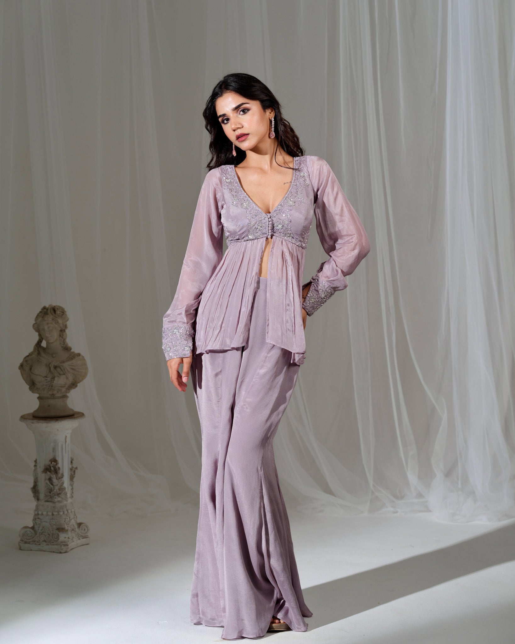 Woman wearing a lavender evening gown with a sheer overlay against a white curtain background